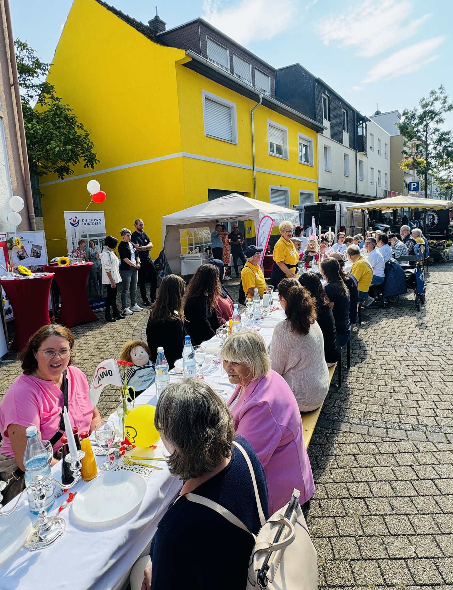 Ehrenamtliche sitzen an einer langen, festlich gedeckten Tafel auf dem Wochenmarktgelände