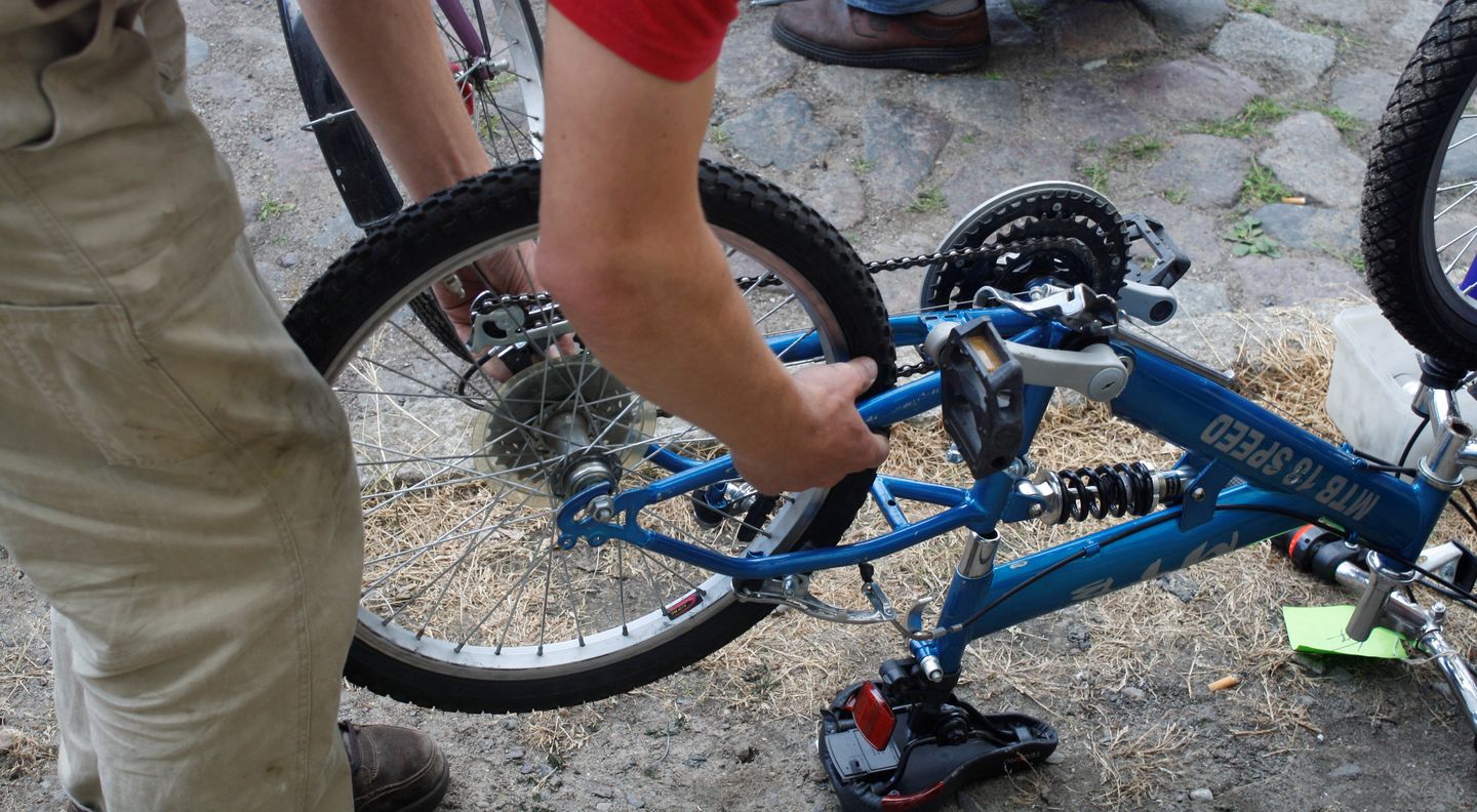ein Fahrrad umgekehrt auf dem Boden stehend, eine Person, die sich darüber beugt und repariert