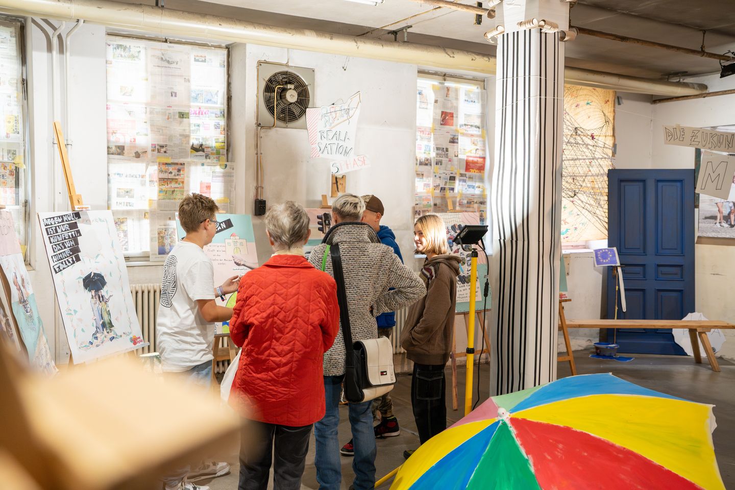 Abgebildet sind Jugendliche, die zwei Erwachsenen ihre Werke erklären.
