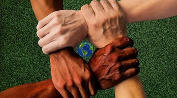 Hände unterschiedlicher Hautfarben greifen einander an den Handgelenken. In ihrer Mitte ist eine Weltkugel.