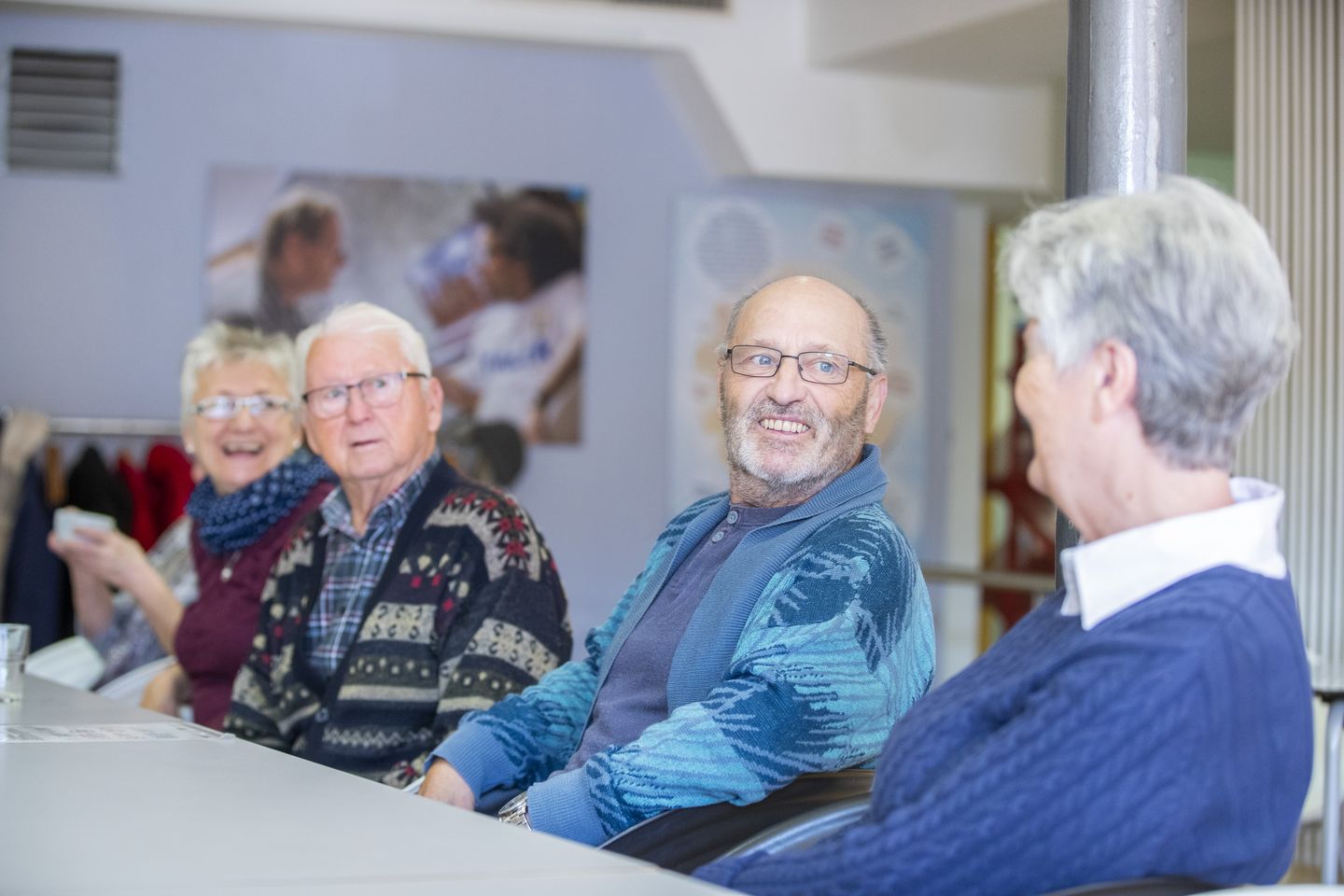 Mehrere Senior*innen sitzen an einem Tisch, unterhalten sich und lachen