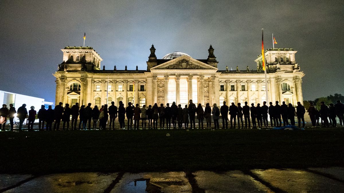 Der beleuchtete Bundestag bei Nacht. Vor dem Gebäude steht eine Menschenkette, die sich dem Gebäude zuwendet.