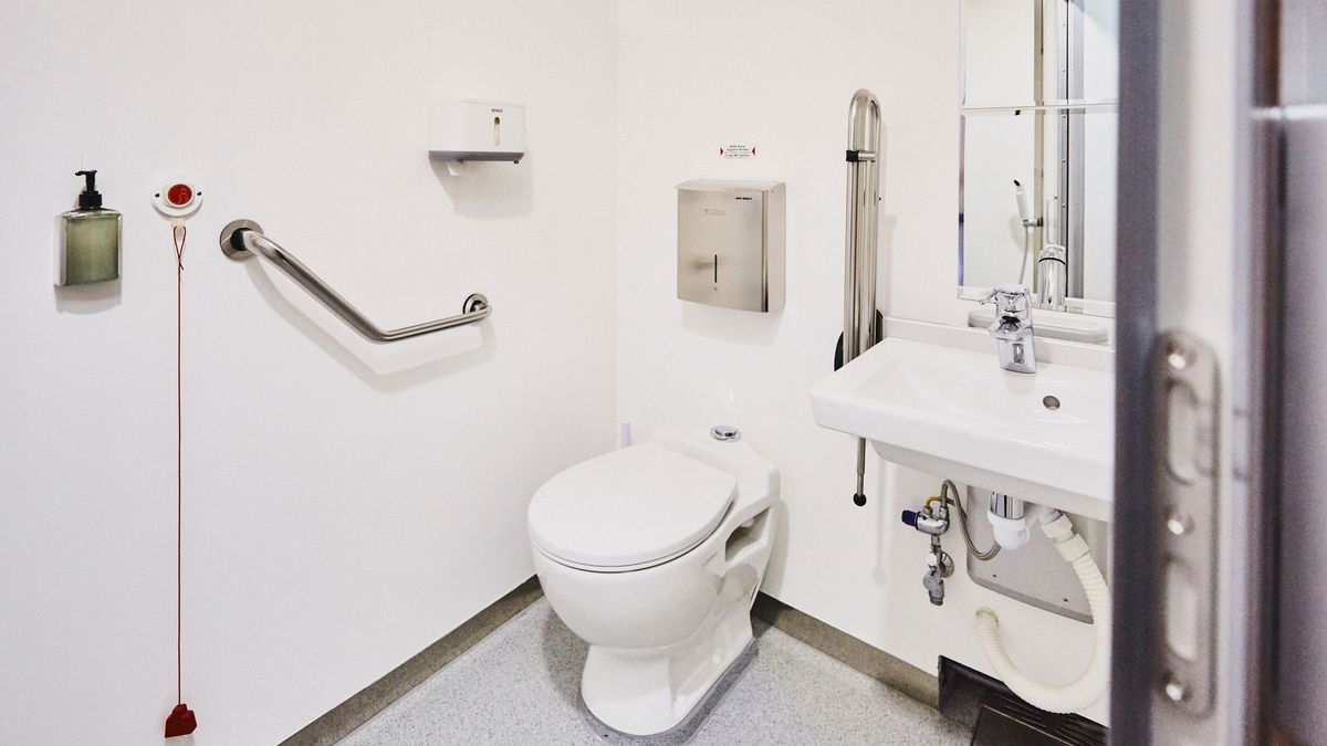 Ein mobiles Badezimmer mit einem Waschbecken sowie einer Toilette. Das Ganze hat Vorrichtungen für behinderte Menschen.  