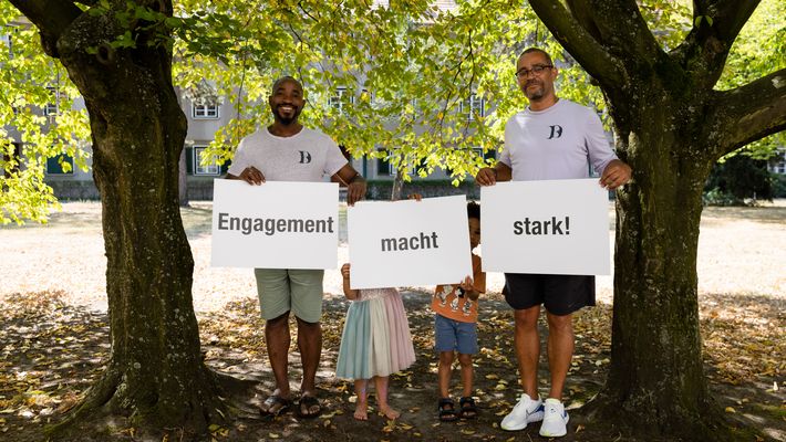Eine Gruppe von Personen steht in Reihen und hält Buchstaben hoch. Die Buchstaben ergeben zusammen den Kampagnen-Slogan “Engagement macht stark!”.