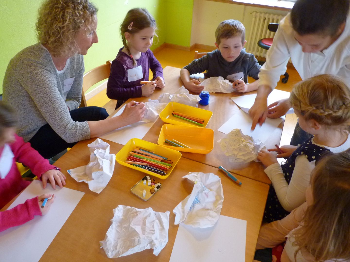 Eine Gruppe von Vorschulkindern probiert unter Anleitung von einer Kritzelpatin und einer Erzieherin Übungen zum Schreibenlernen aus.