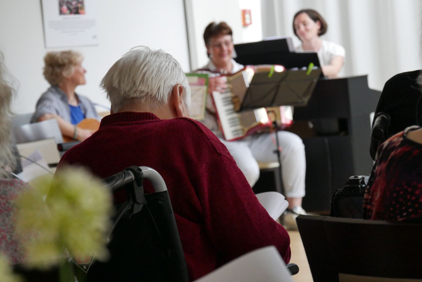 Musikerinnen machen auf einer Bühne Musik. Von hinten sieht man einen älteren Herren, der der Musik zuhört.
