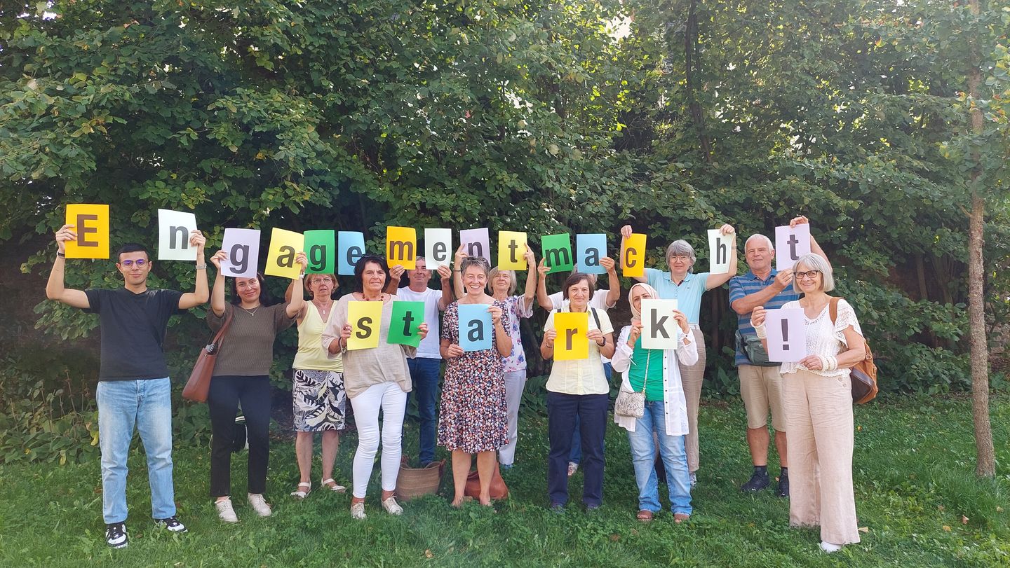 Ehrenamtlich Engagierte des Mehrgenerationenhauses Bad Kissingen stehen im Grünen und halten den Schriftzug "Engagement macht stark!" hoch!