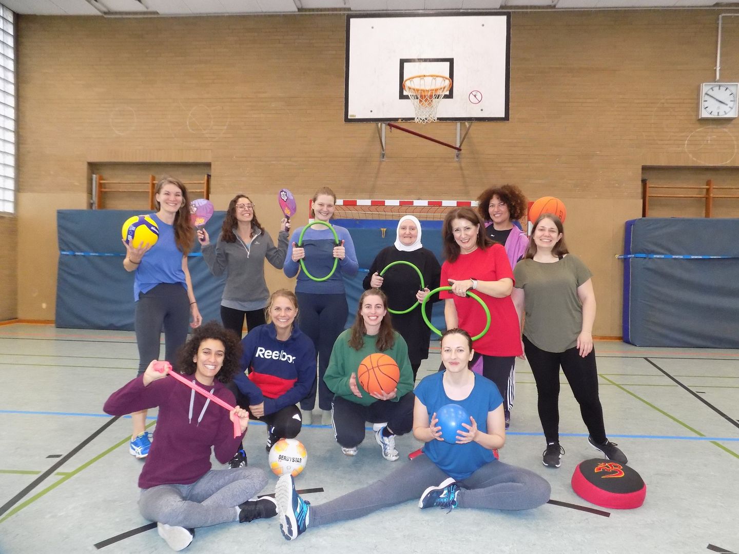 Frauen vom Team von Move and Meet stehen in einer Gruppe  mit Sportgeräten in der Hand in einer Sporthalle.