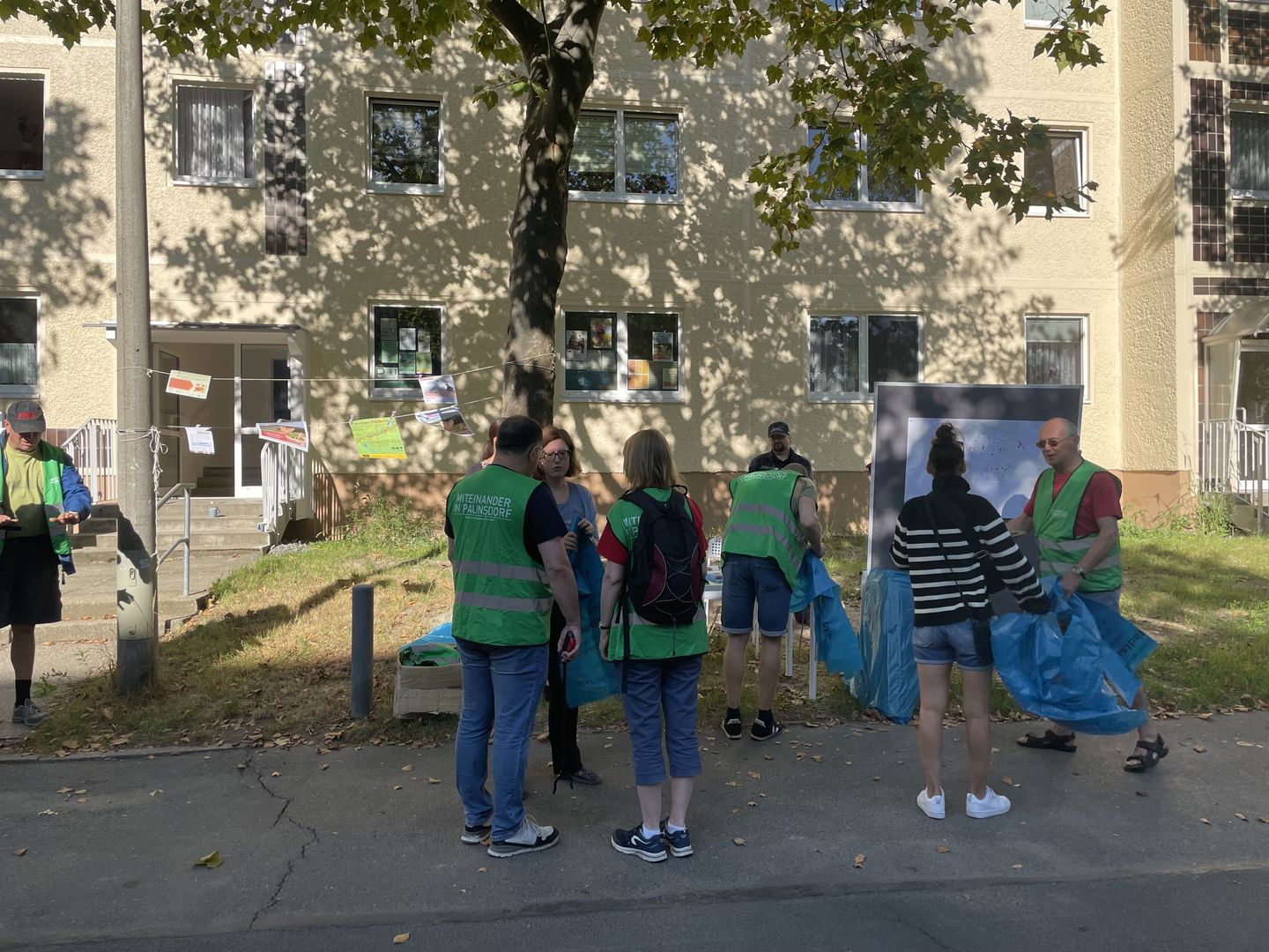 mehrere Menschen erhalten Mülltüten und Greifer, im Hintergrund ein Wohnhaus