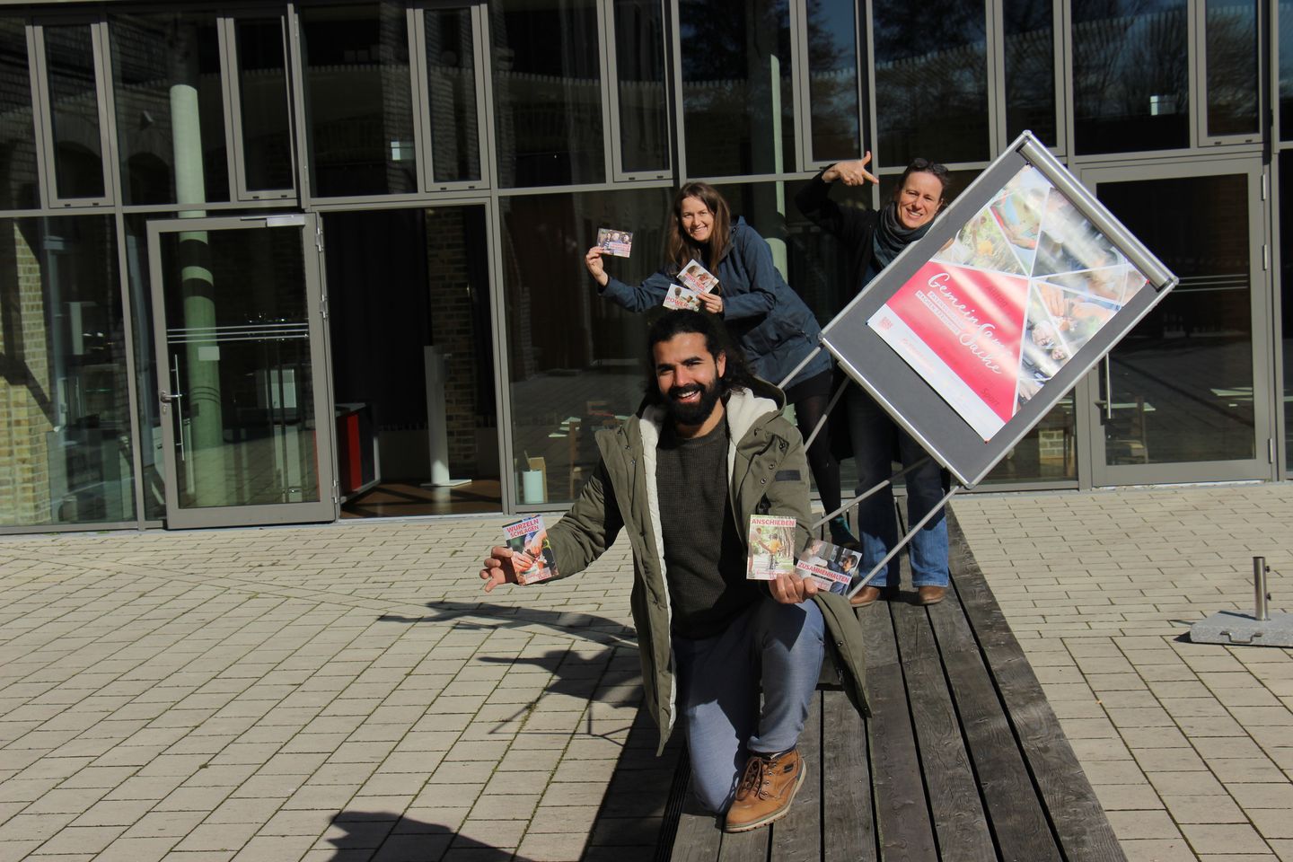 zwei Frauen und ein Mann mit einem Plakat vor dem Café
