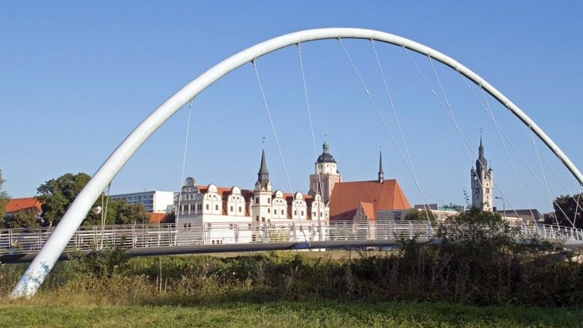 Weißer Brückenbogen mit einem Stadtpanorama im Hintergrund. 