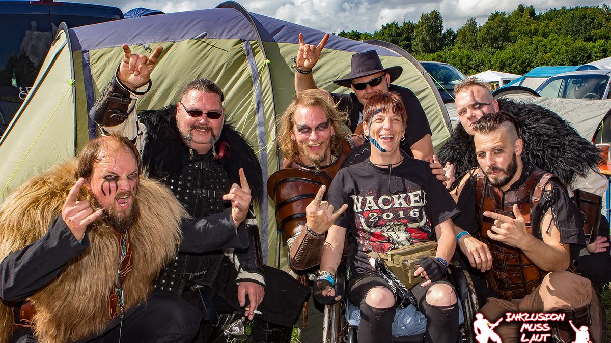 Metal-Fans mit und ohne Rollstuhl posieren auf einem Campingplatz.