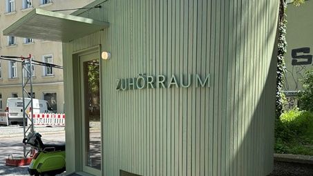 Ein kleines grünes Gebäude, auf dem "Zuhörraum"
