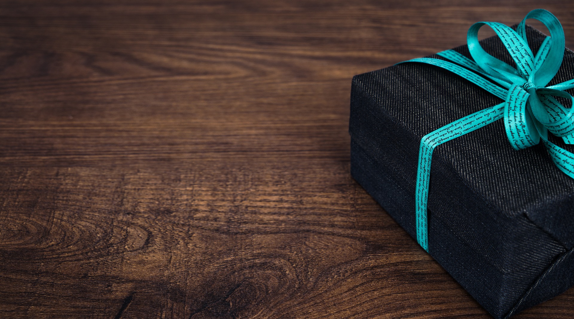 Schwarzes Geschenkpaket mit hellblauer Schleife auf dunklem Holztisch.