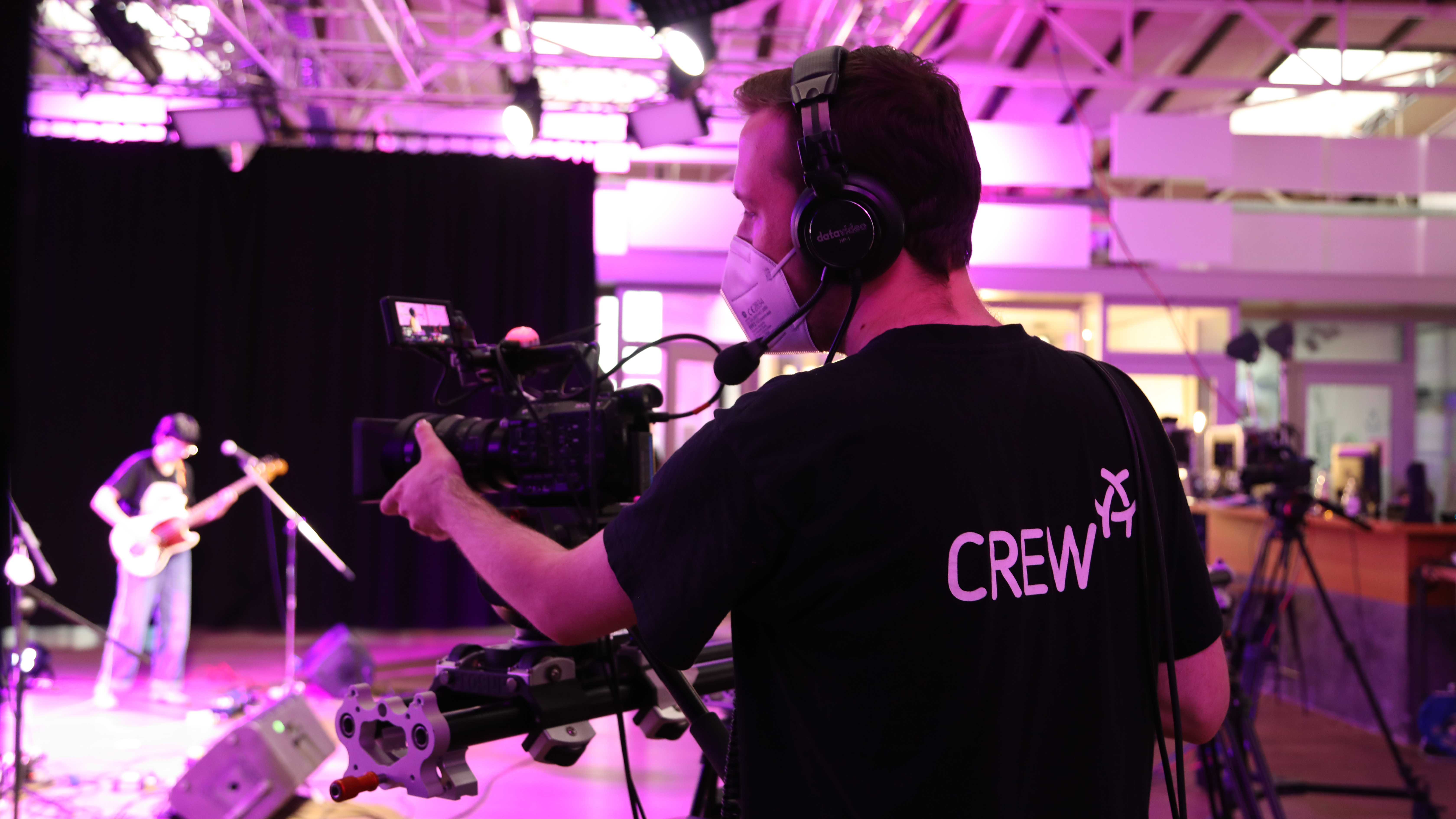 TV-Studio-Situation: Im Vordergrund bedient ein Mitarbeiter von Alex Berlin eine Kamera. Im Hintergrund steht ein Mensch mit Gitarre und Mikrofon auf einer Studio-Bühne.