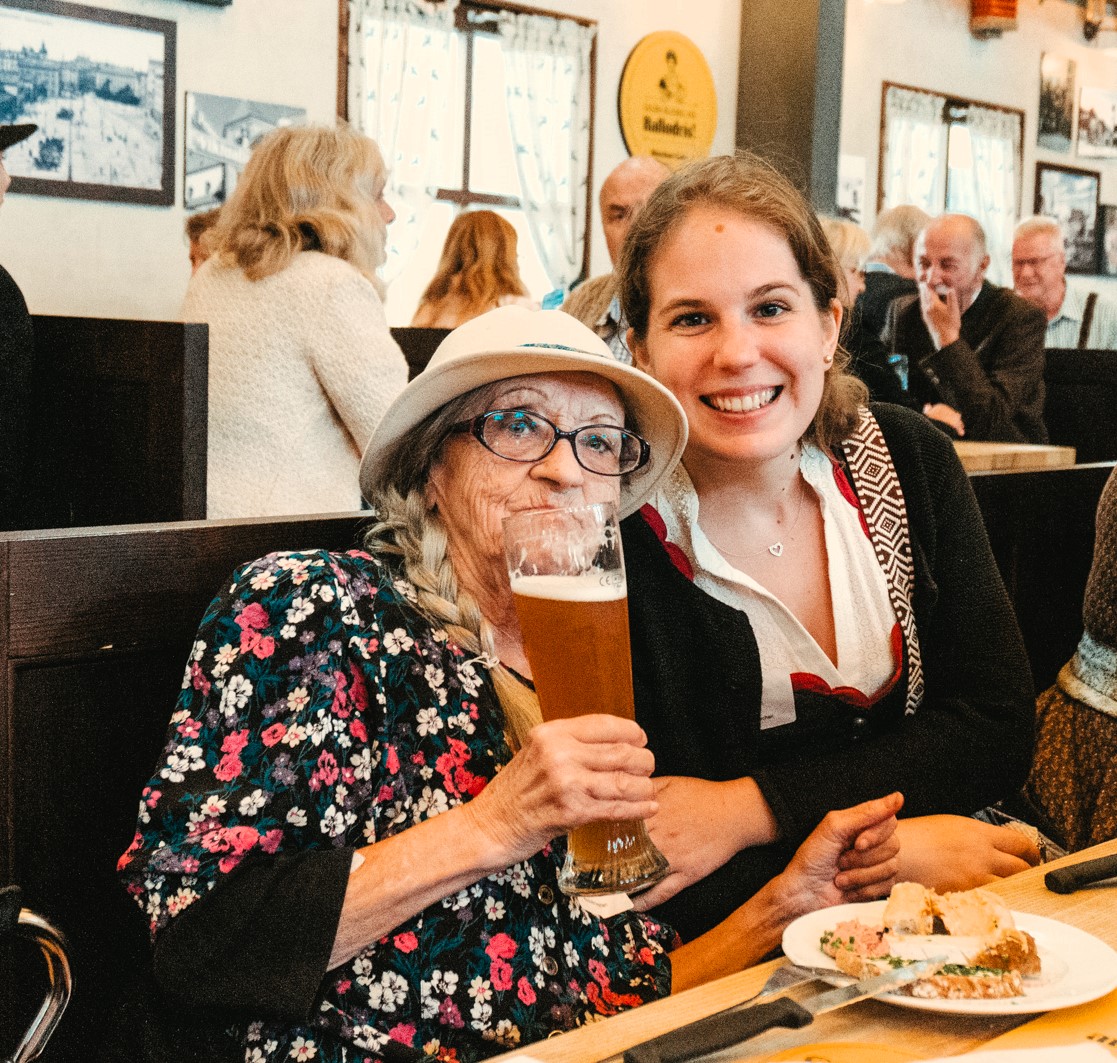 Auf dem Foto ist eine ältere Dame und eine jüngere Dame, die eng beieinander auf einer Bierbank im Wiesn-Zelt sitzen.