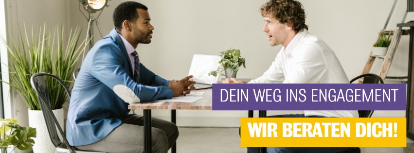 Zwei Männer sitzen sich an einem Tisch gegenüber und unterhalten sich. Links ein Mann im blauen Anzug, rechts ein Mann im weißen Hemd. Auf dem Tisch liegen Unterlagen und eine kleine Pflanze. Im Hintergrund sind weitere Pflanzen und eine Leiter zu sehen. Auf dem Bild steht der Text: „Dein Weg ins Engagement – Wir beraten dich!