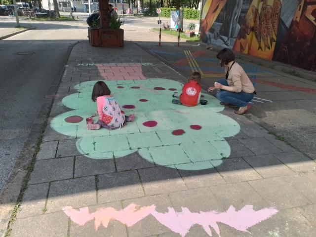 Kinder malen  auf den Asphalt rote Kirschen auf einen grünen Baum